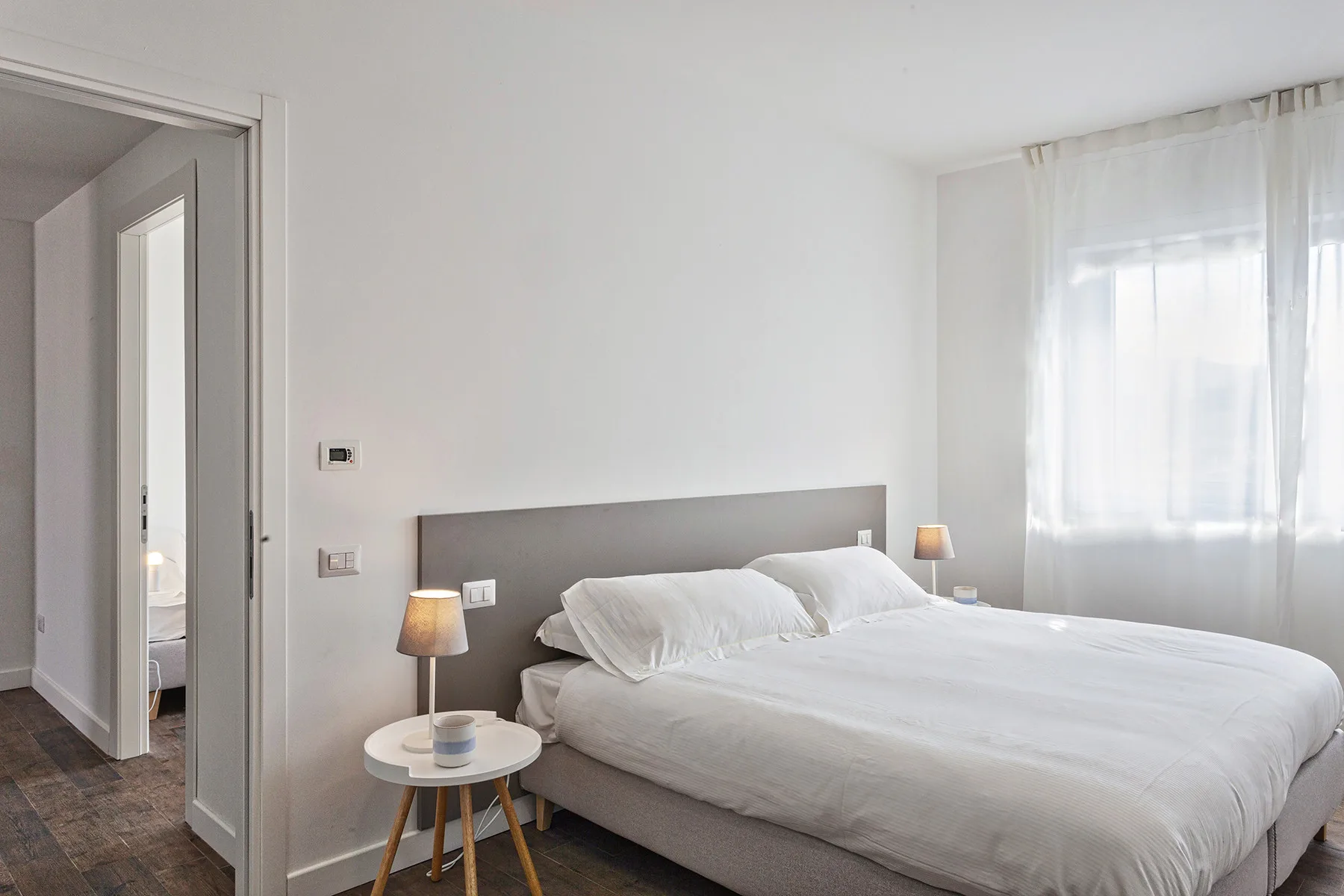 Un dormitorio luminoso con una cama bien tendida y una ventana grande con cortinas.