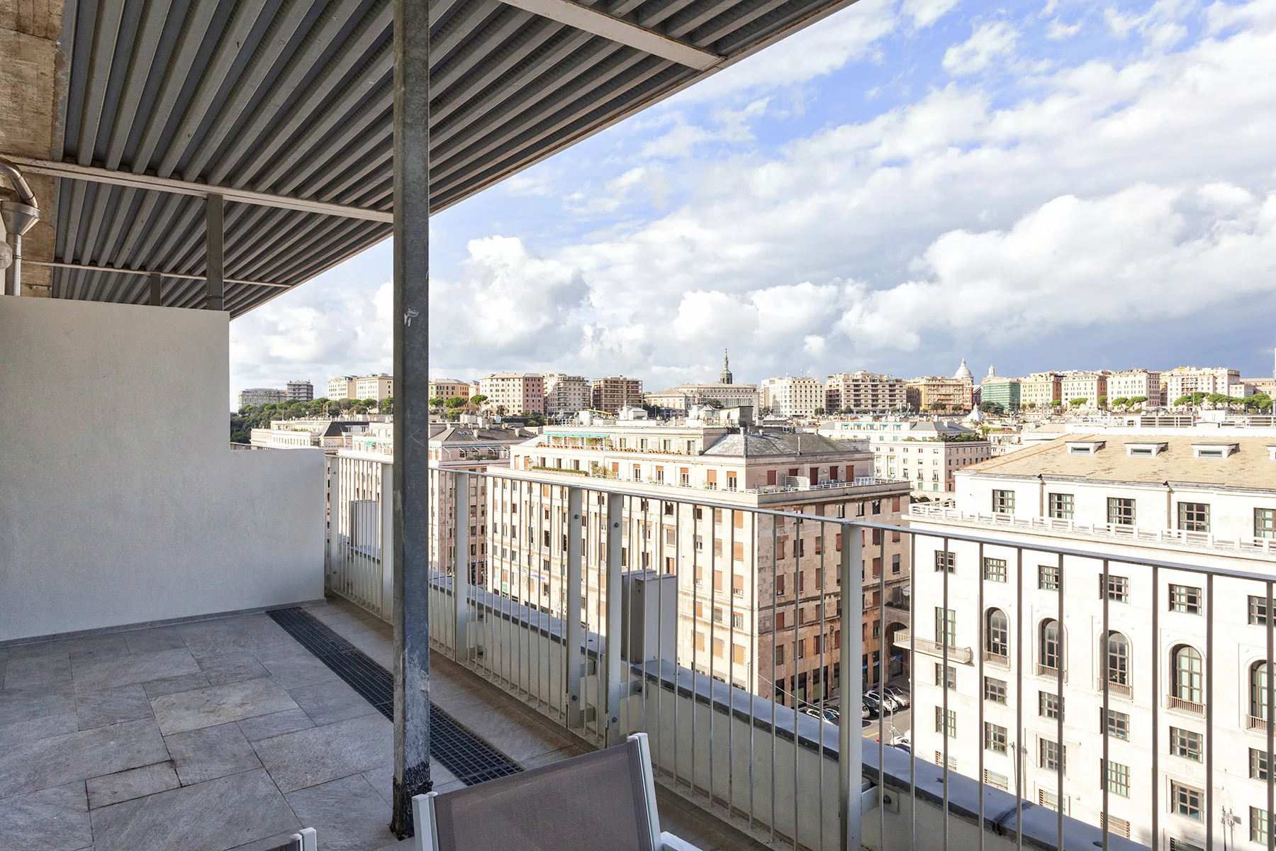 Un balcón cubierto ofrece vistas de edificios de la ciudad bajo un cielo parcialmente nublado.