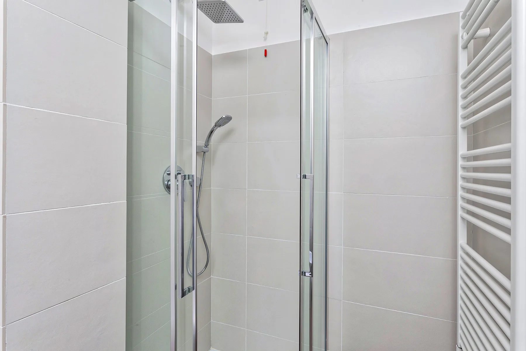 Una ducha de baño con azulejos, ducha de mano y toallero calefactor en la pared.