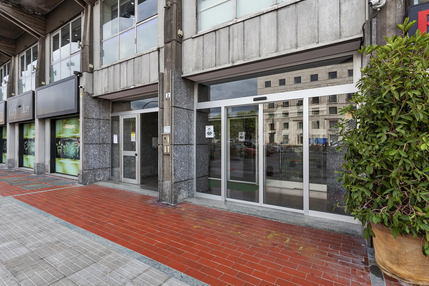Entrada a un edificio a nivel de calle, con puertas de vidrio y acera de ladrillo.
