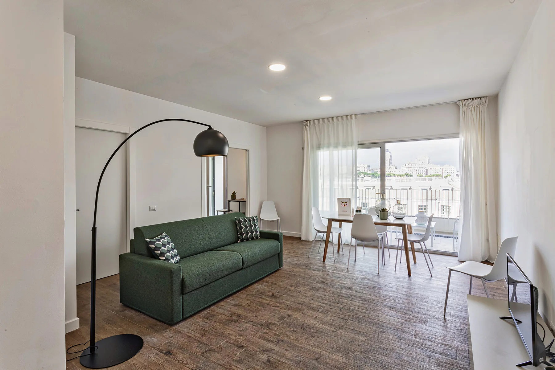 Una luminosa sala de estar y comedor con asientos verdes y una mesa junto a grandes ventanas.