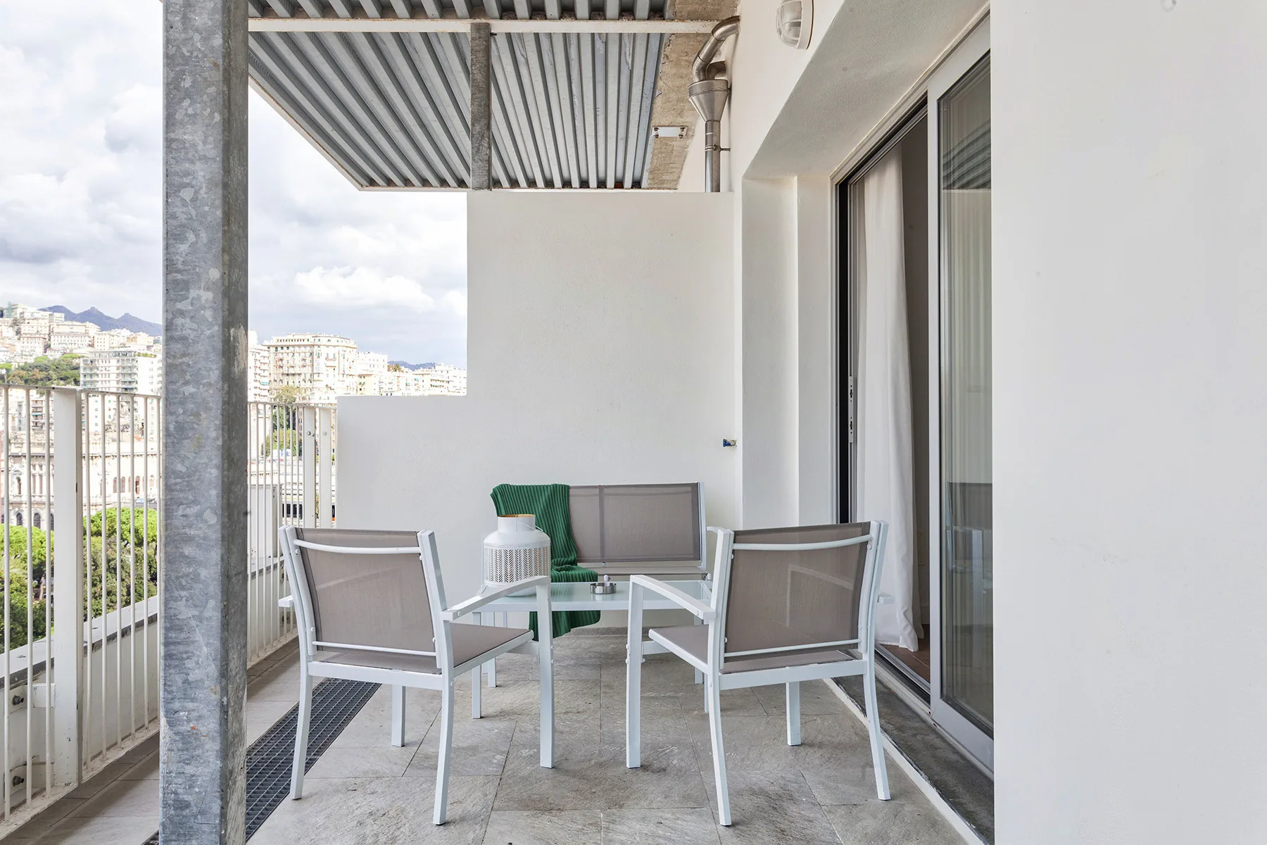 Zona de estar en un balcón con una mesa pequeña y vistas de la ciudad tras la barandilla.
