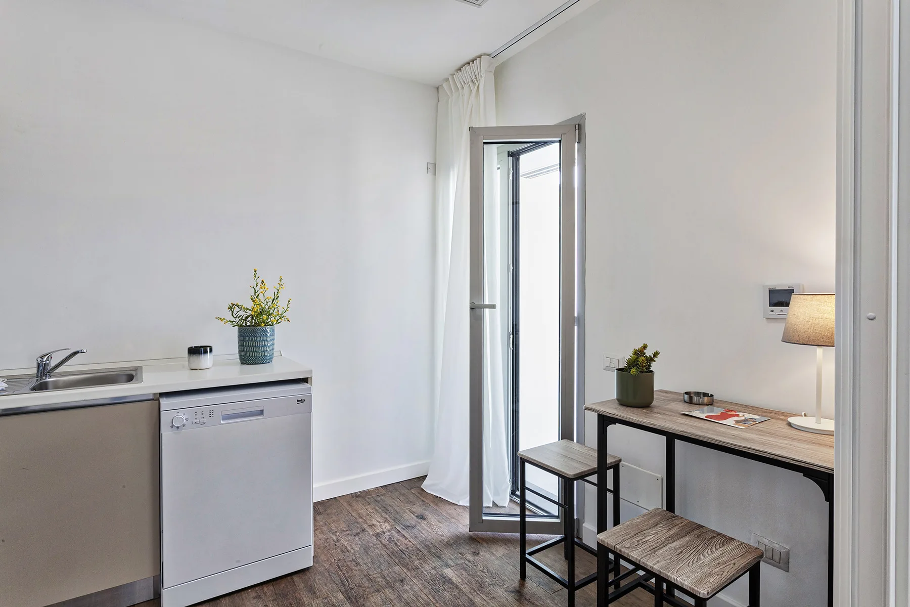 Una cocina pequeña y zona de comedor luminosa con encimera, mesa y taburetes.