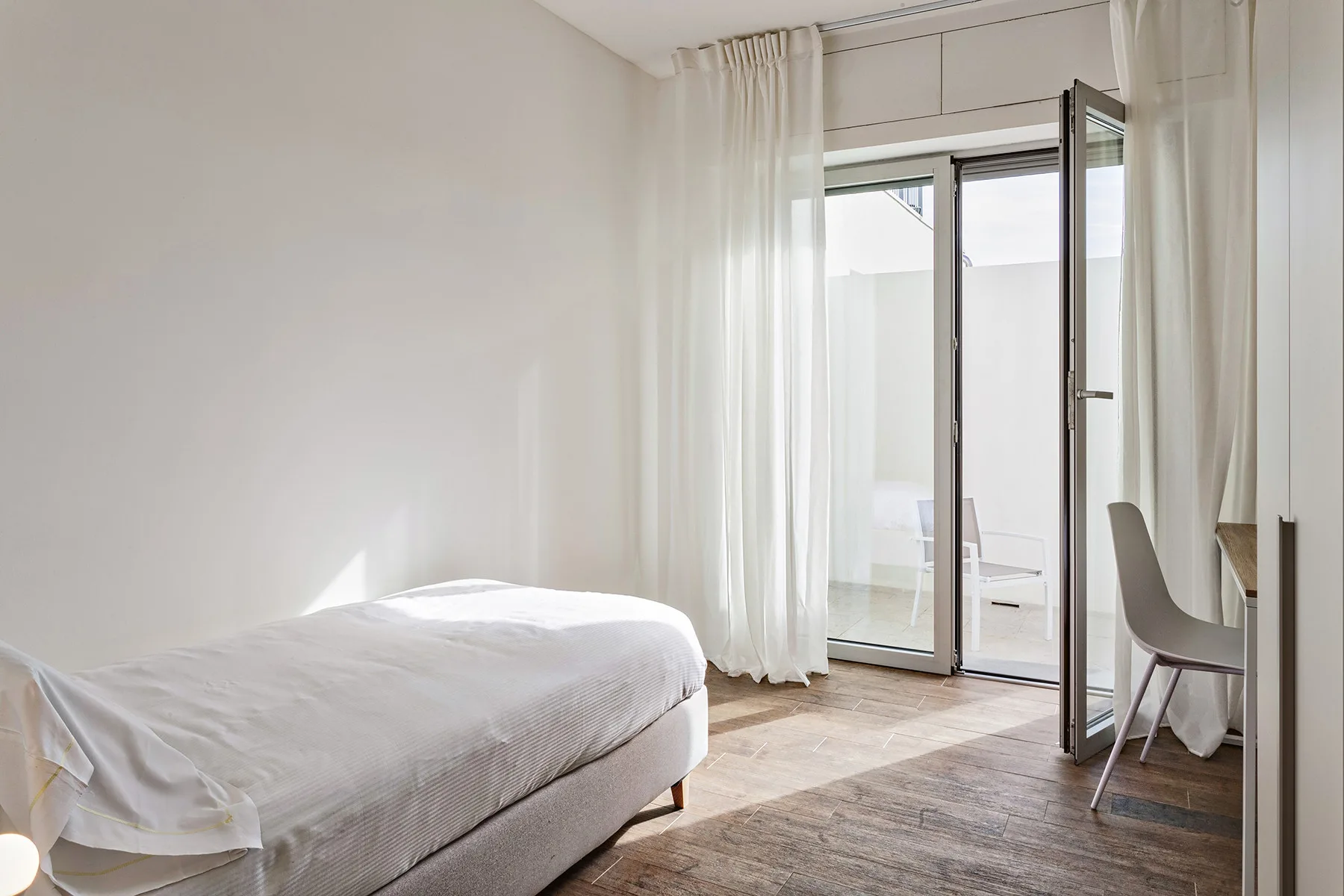 Un dormitorio luminoso con una cama junto a puertas de vidrio abiertas y cortinas.