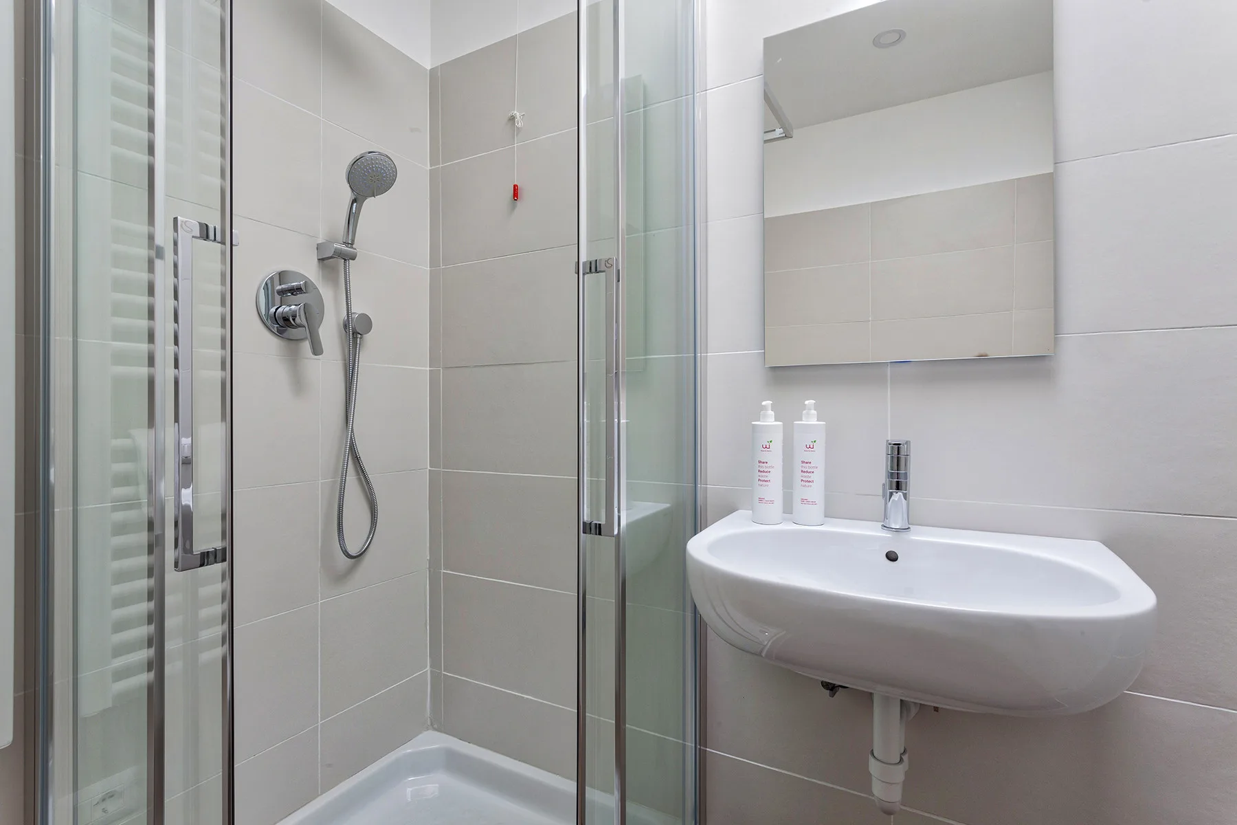 Un baño alicatado con ducha de vidrio y lavabo de pared.