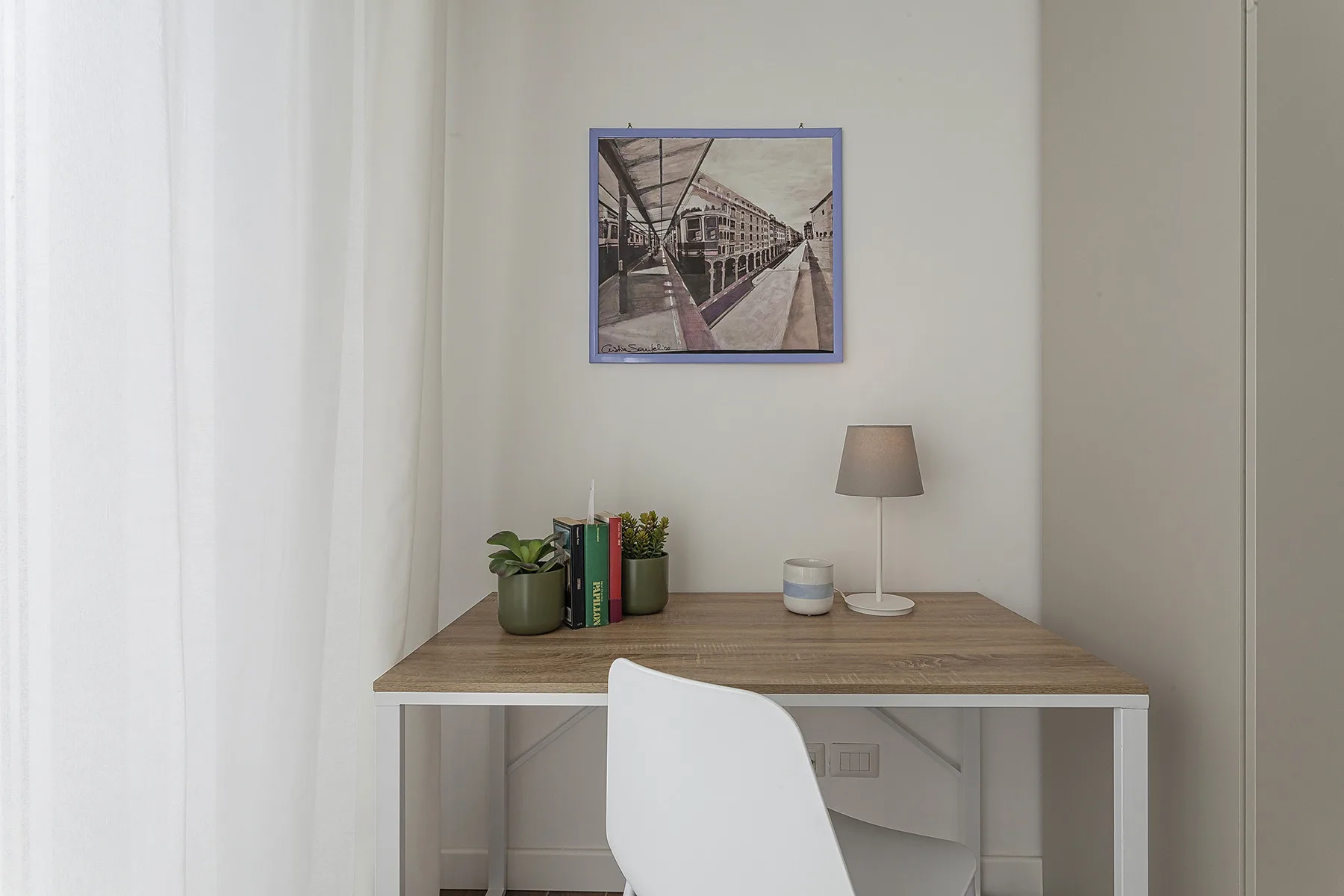 Un escritorio está junto a una pared clara, con un cuadro enmarcado encima.