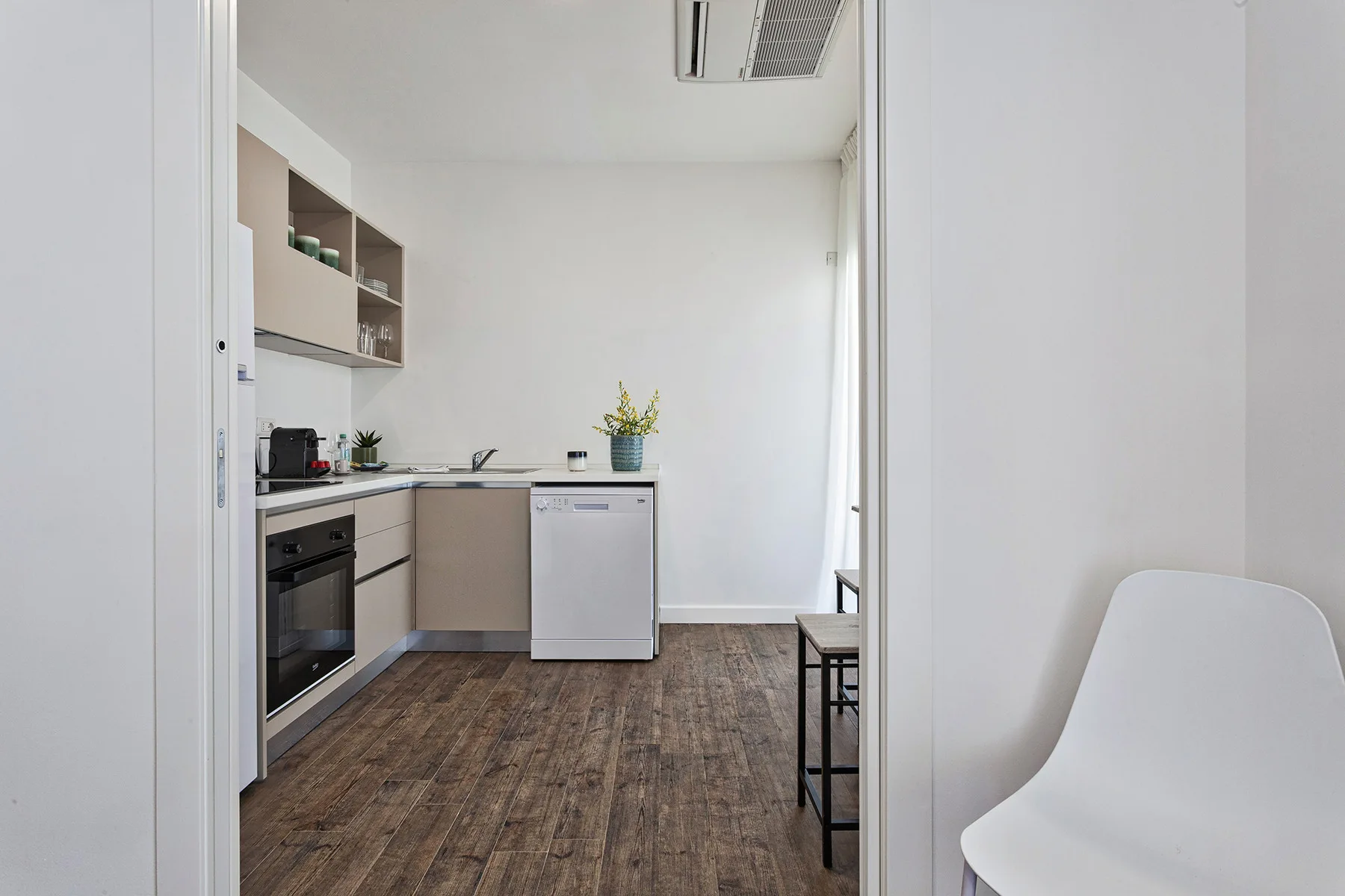 Una cocina compacta con gabinetes claros, electrodomésticos sobre la encimera y una planta pequeña.