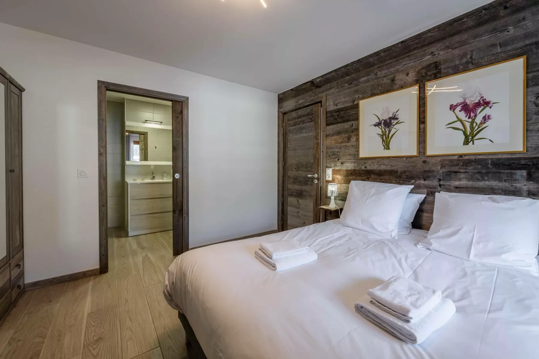 A bedroom with a large bed, white bedding, and framed floral artwork.