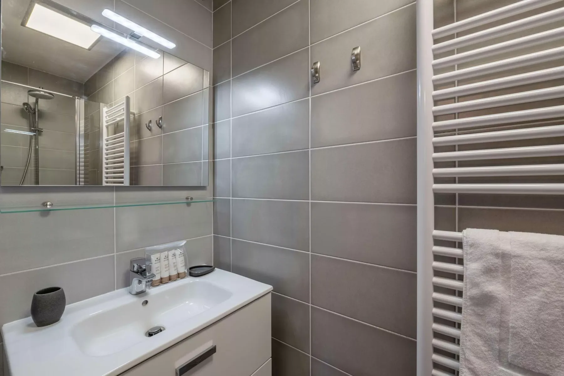 A tiled bathroom with a sink, wall mirror, and towel warmer.