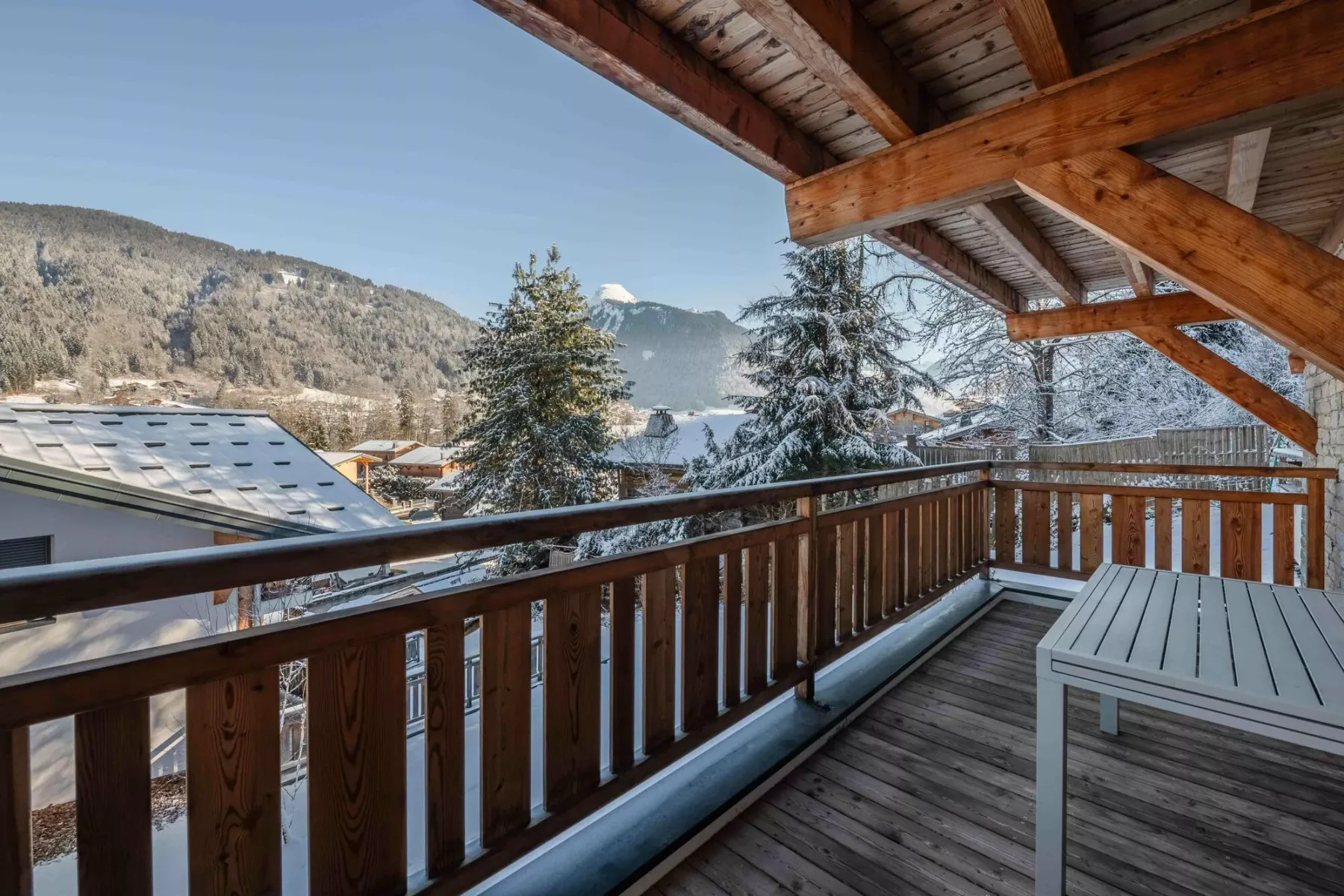 A covered wooden balcony overlooks snow-covered rooftops and a mountain landscape.