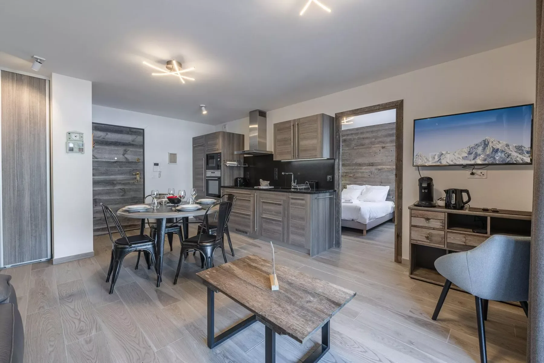 An open-plan living area with a dining table, kitchen, and bedroom doorway.