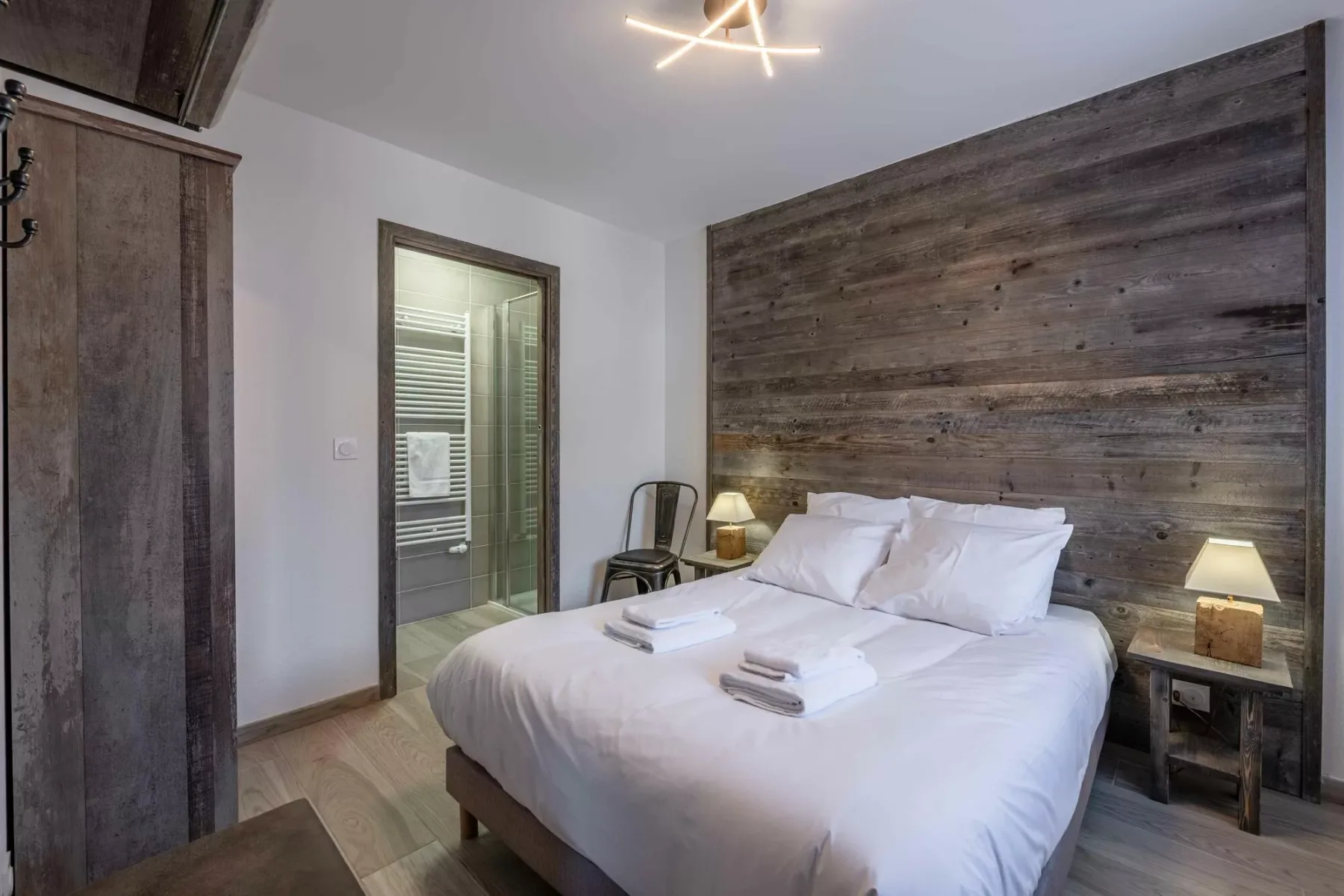 A bedroom with a neatly made bed and a dark wood-paneled wall.