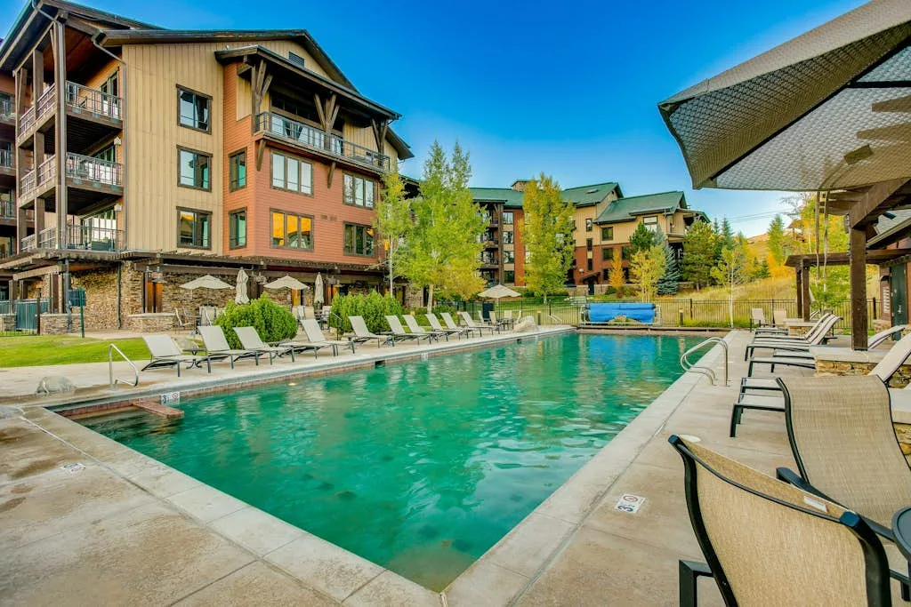 Una piscina al aire libre junto a un edificio de varios pisos, con asientos en la terraza.