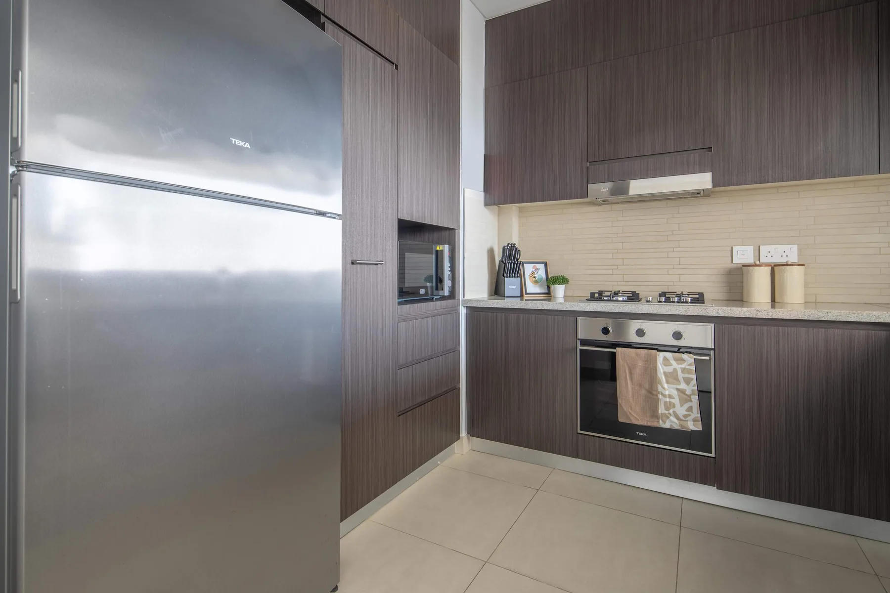 A modern kitchen with dark cabinetry, a stainless-steel refrigerator, and a tiled backsplash.