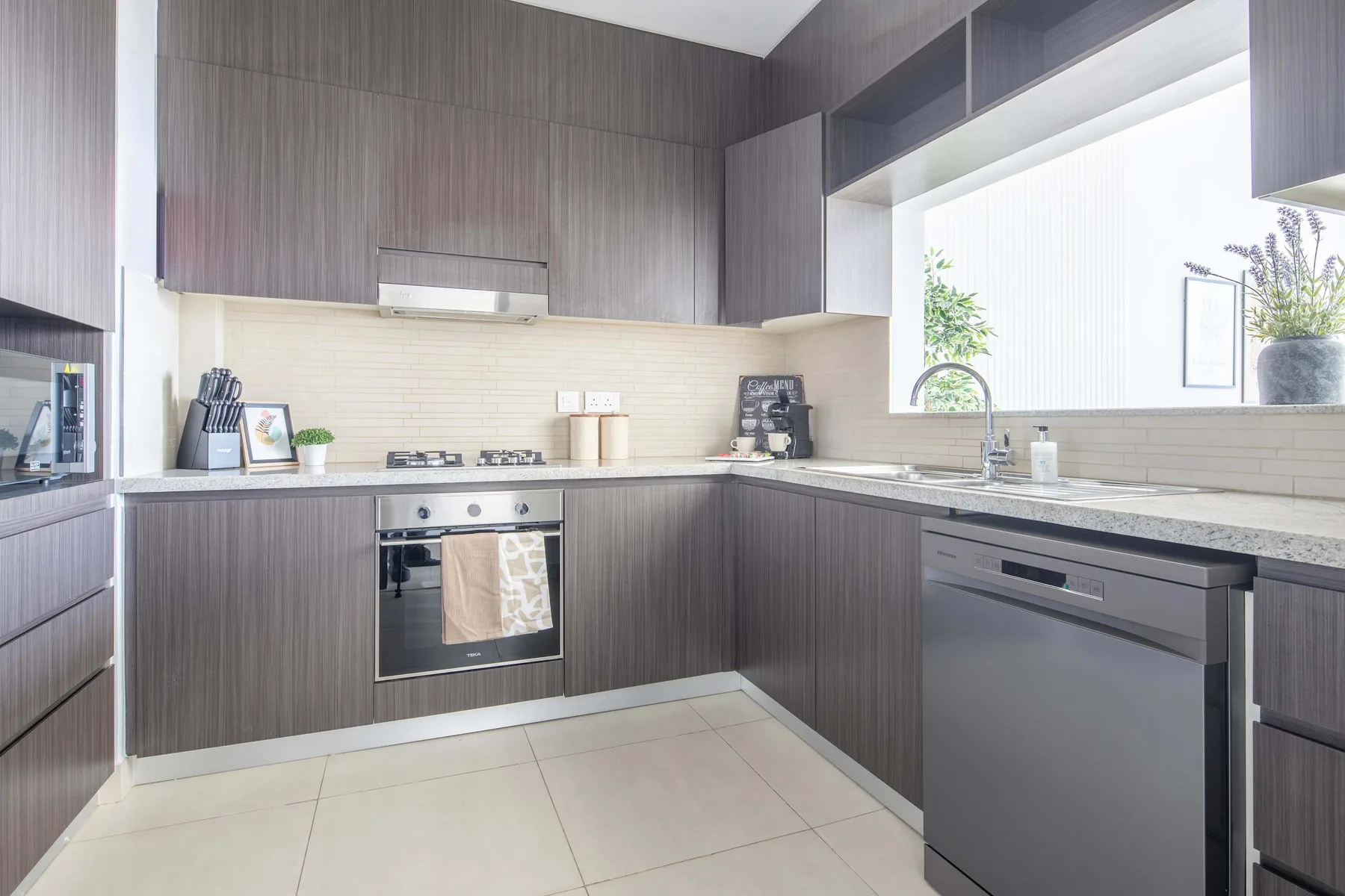 A modern kitchen with dark cabinets, a countertop, and a large window.