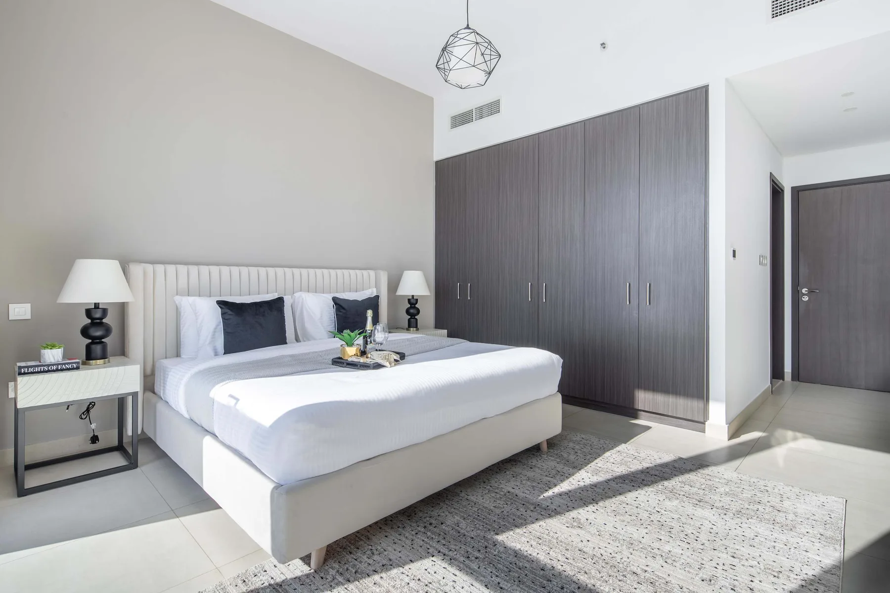 A bright bedroom with a neatly made bed and dark built-in wardrobes.
