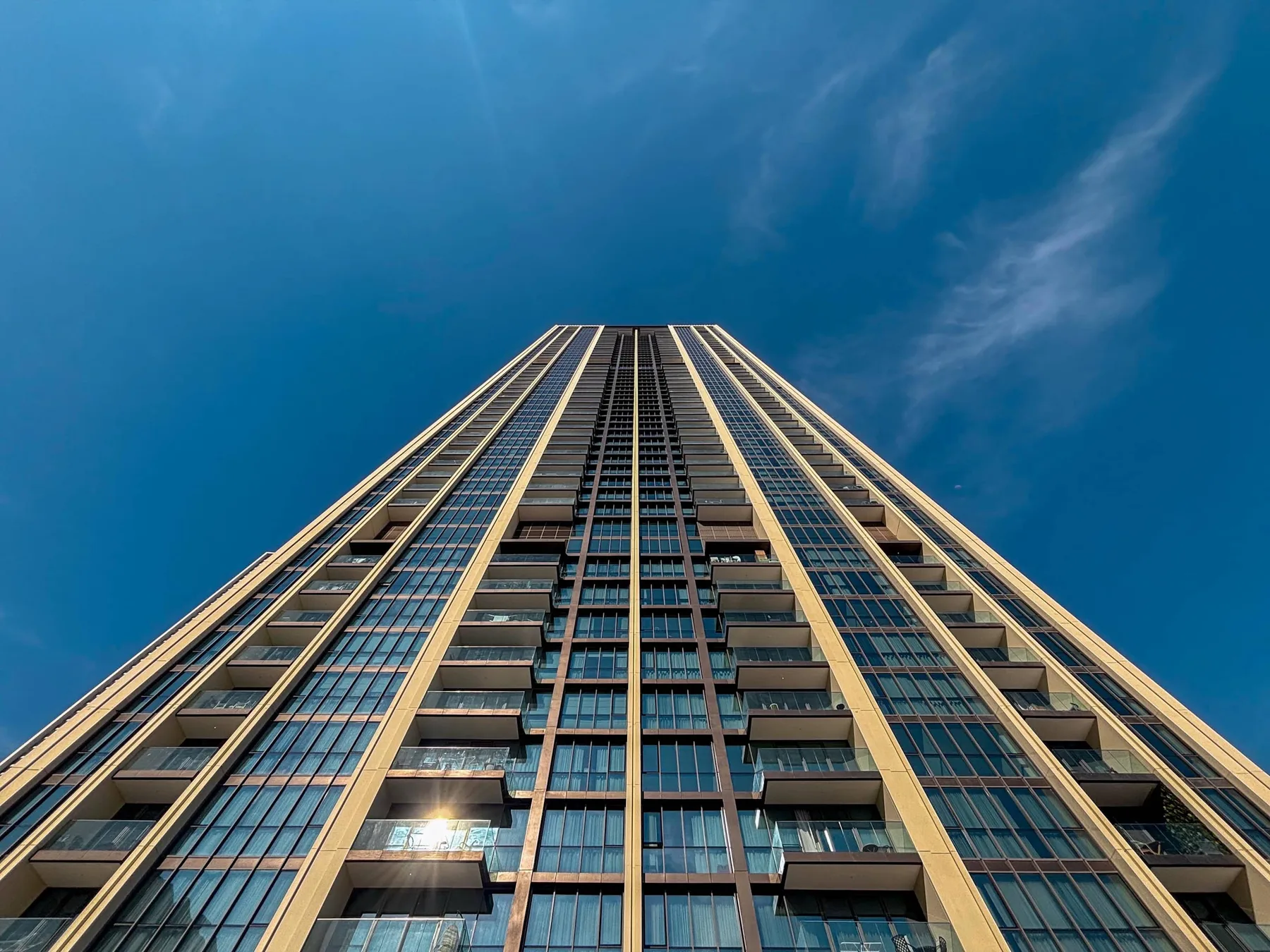 A tall glass-fronted building rises against a blue sky.