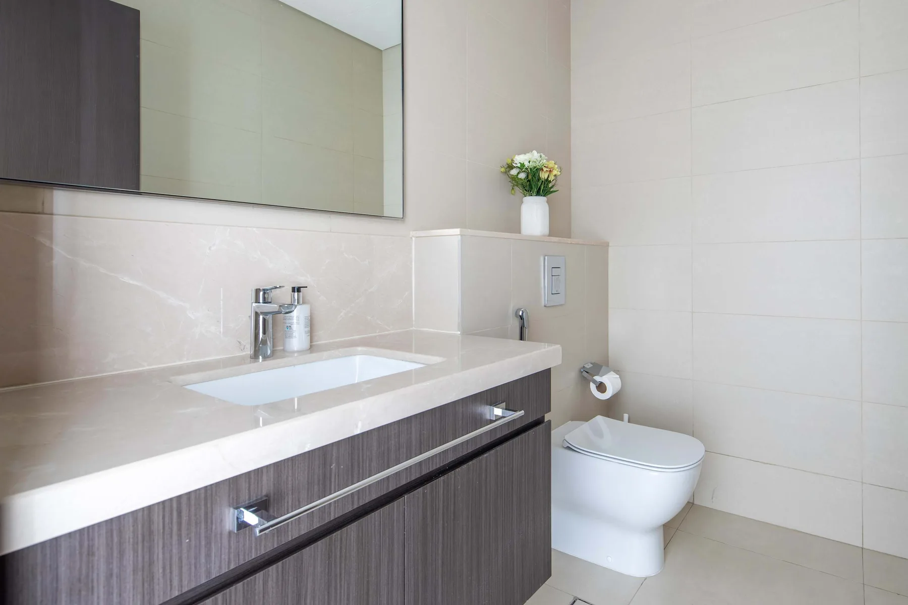 A tiled bathroom with a sink vanity, mirror, and toilet.