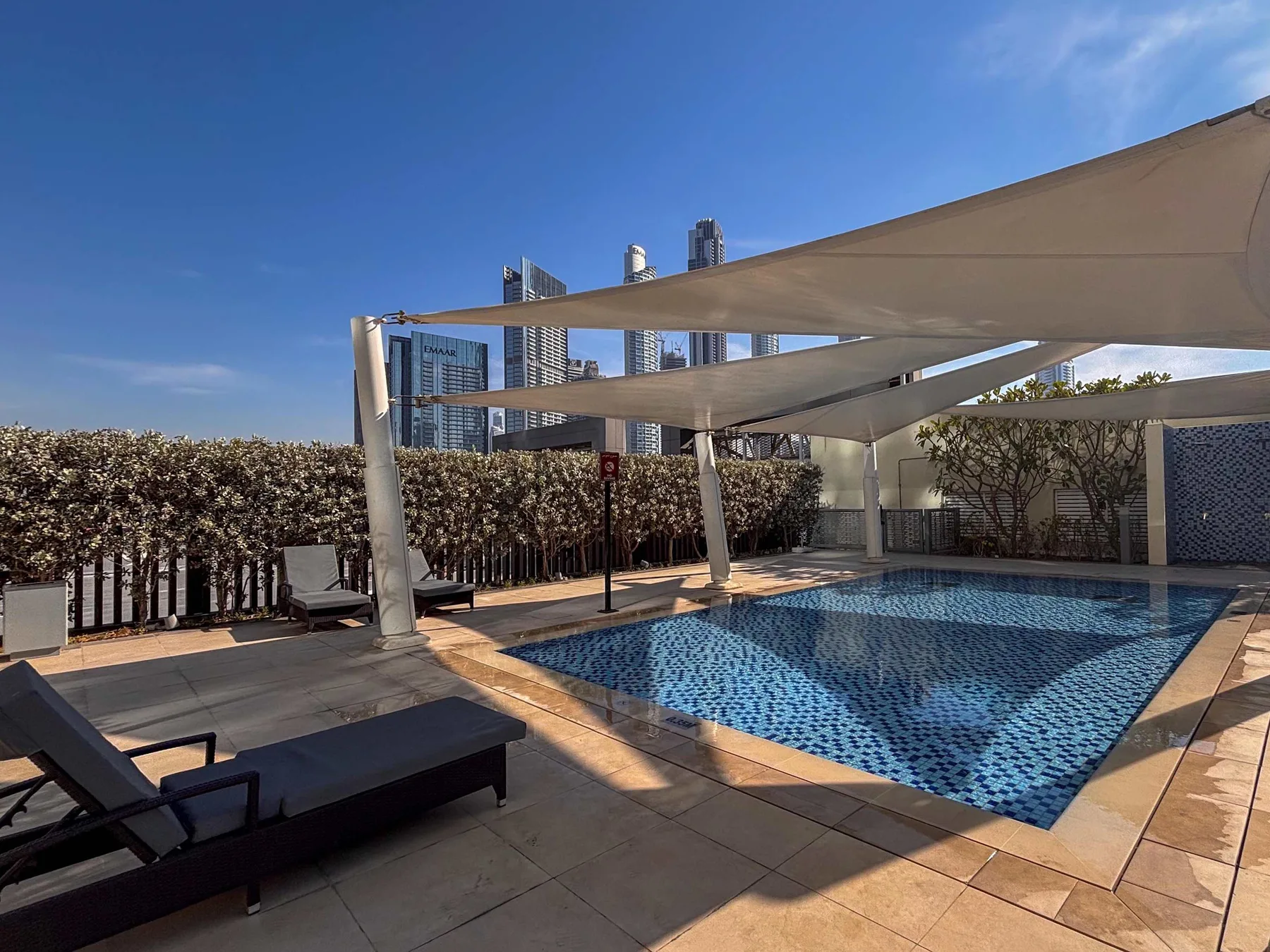An outdoor swimming pool sits beneath shade canopies, with lounge seating beside it.
