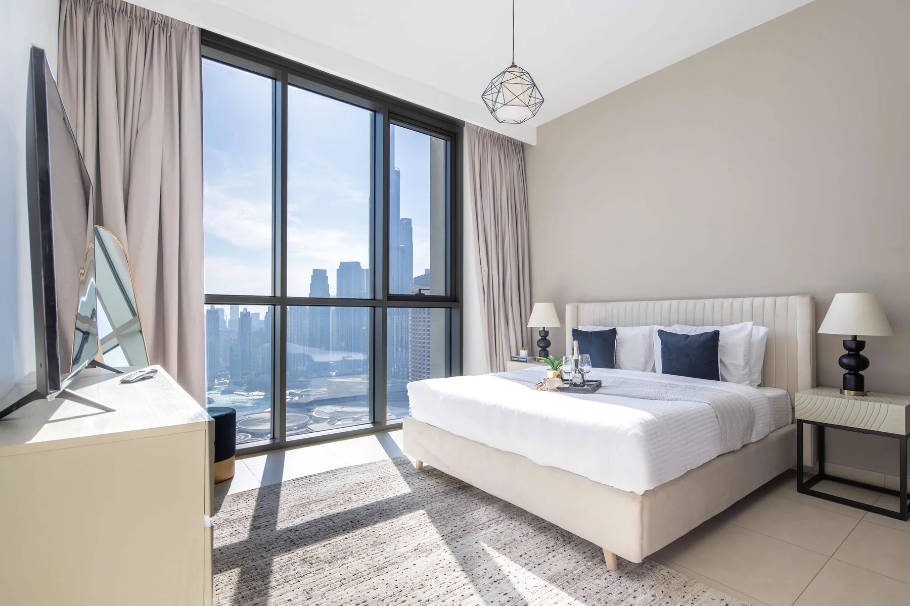 A bright bedroom with a neatly made bed beside large windows.
