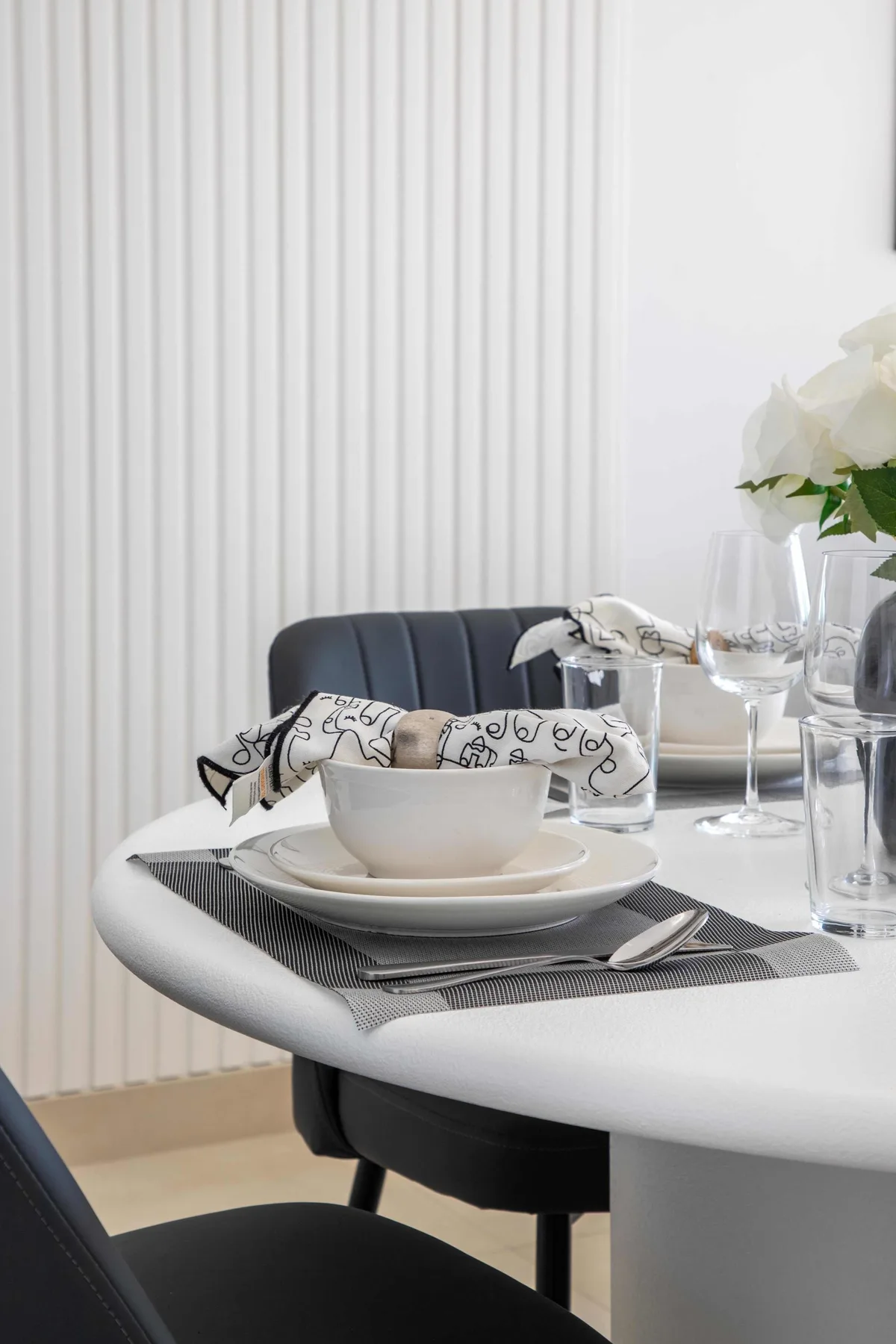 A dining table is set with dishes and glassware beside a white floral arrangement.