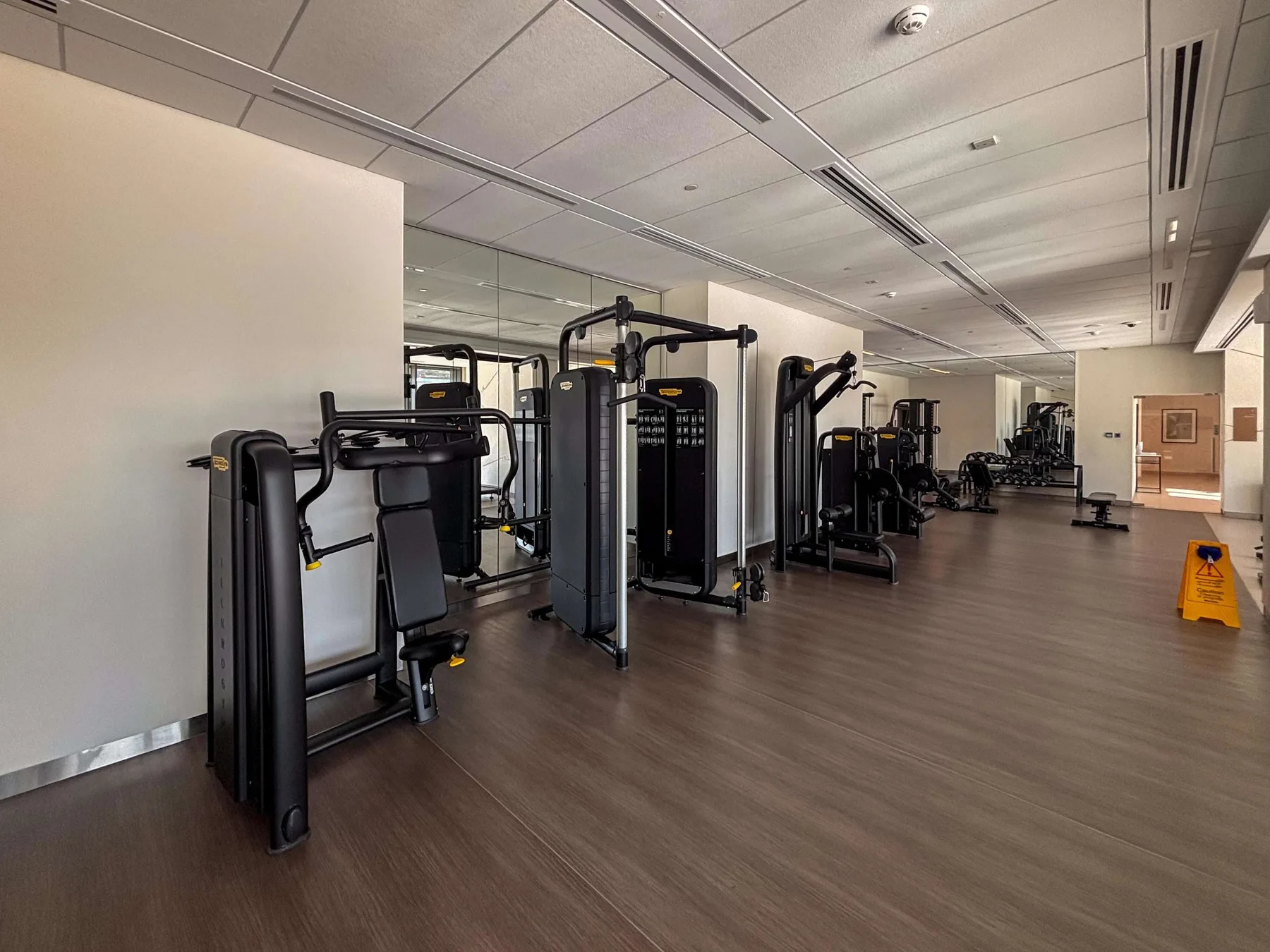 A gym with rows of exercise machines on a dark floor.
