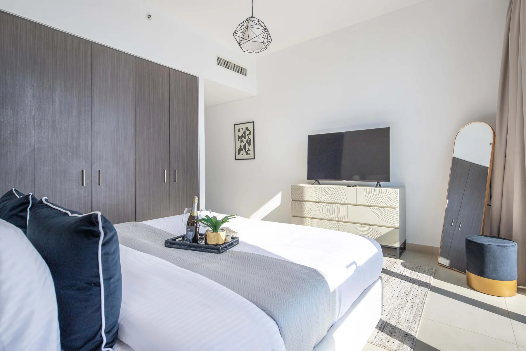 A bright bedroom with a bed, dark wardrobes, and a television on a dresser.