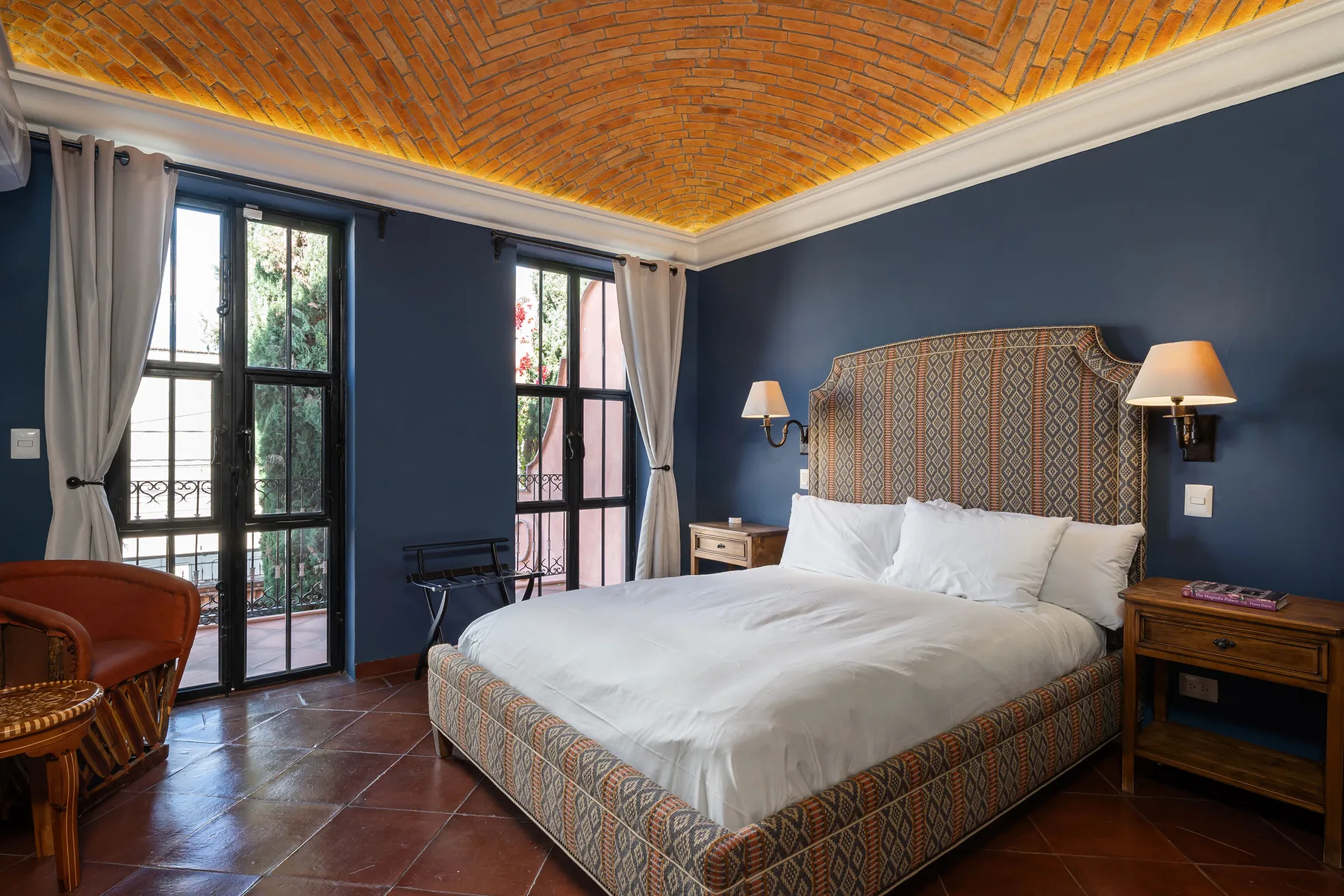 A bedroom with a large bed, dark blue walls, and tall windows.