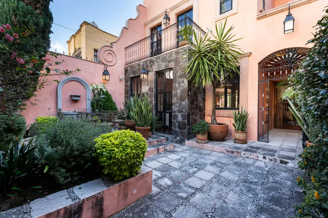 A paved courtyard with potted plants sits beside a pink building.
