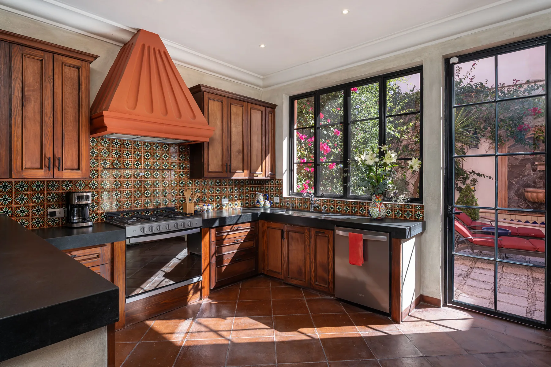 A kitchen with wooden cabinets, patterned tile, and large windows overlooking a garden.