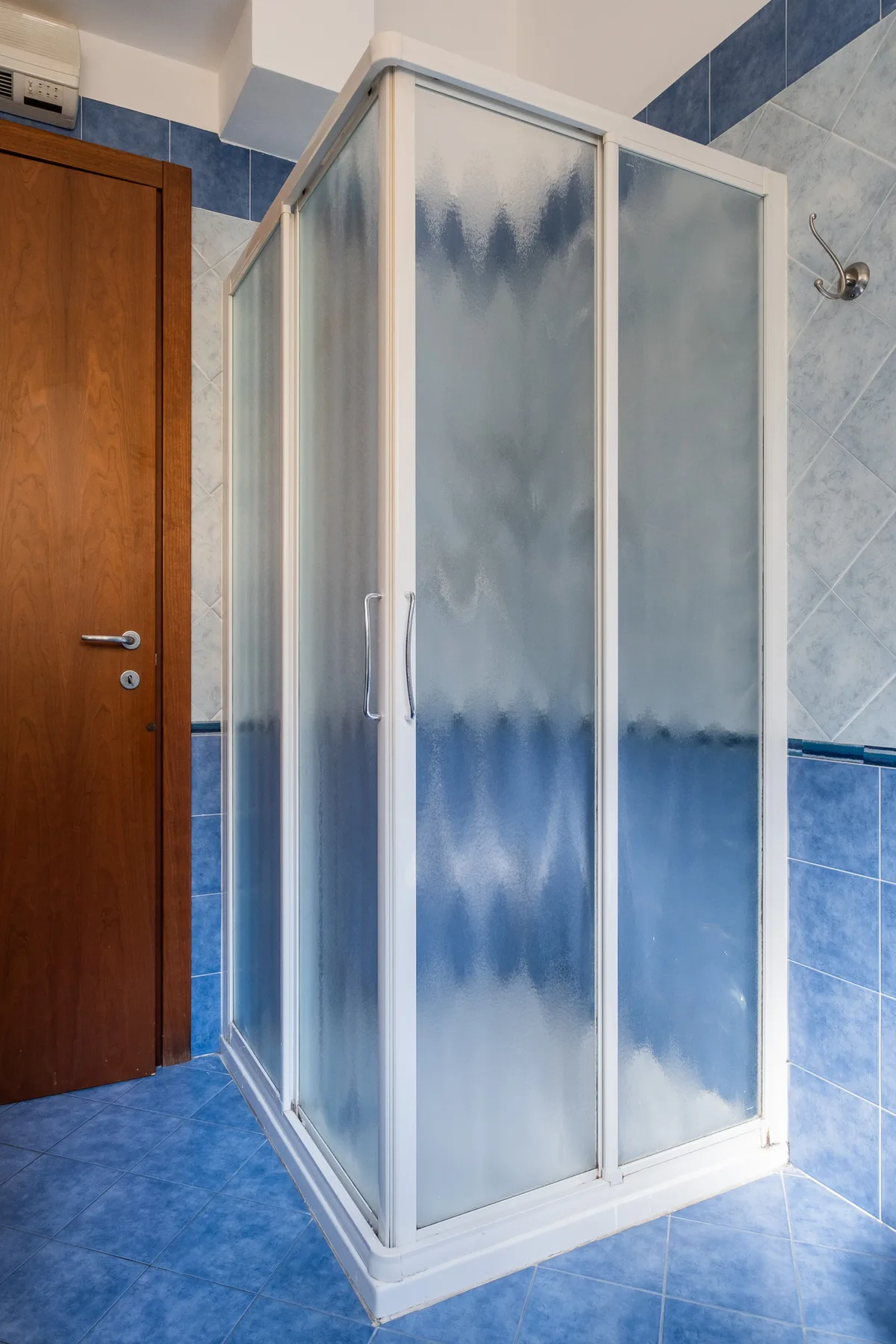 Una ducha de baño con paneles de vidrio esmerilado y paredes de azulejos azules.