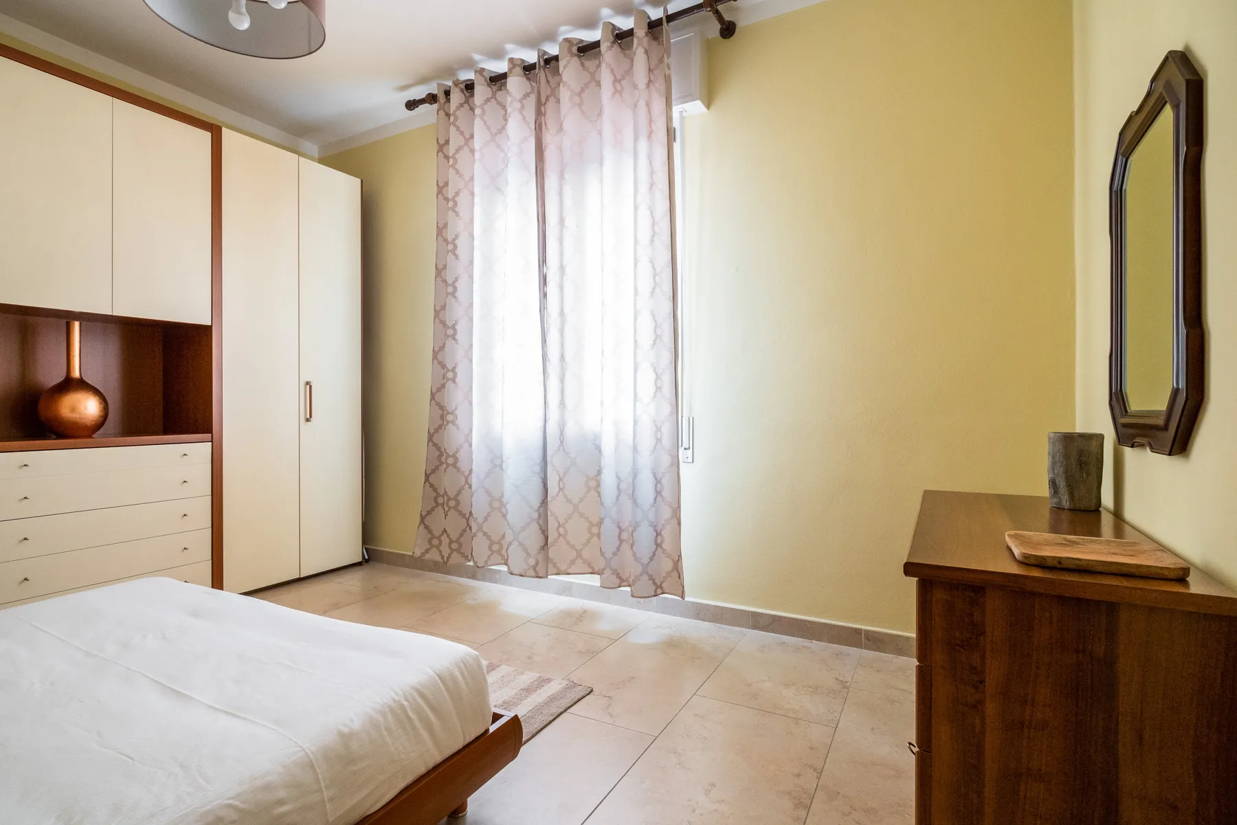 Un dormitorio con una cama, un armario y una ventana con cortinas.