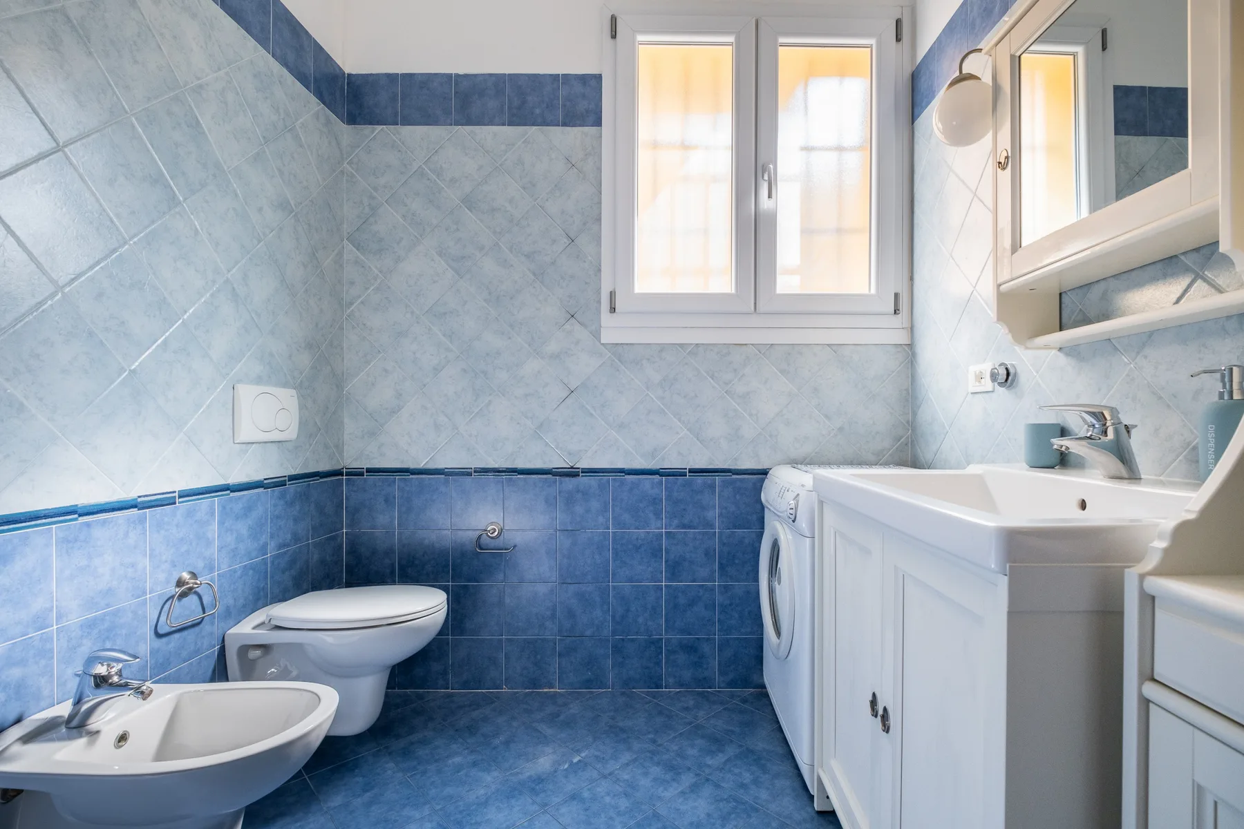 Un baño alicatado con inodoro, bidé, lavabo y lavadora.