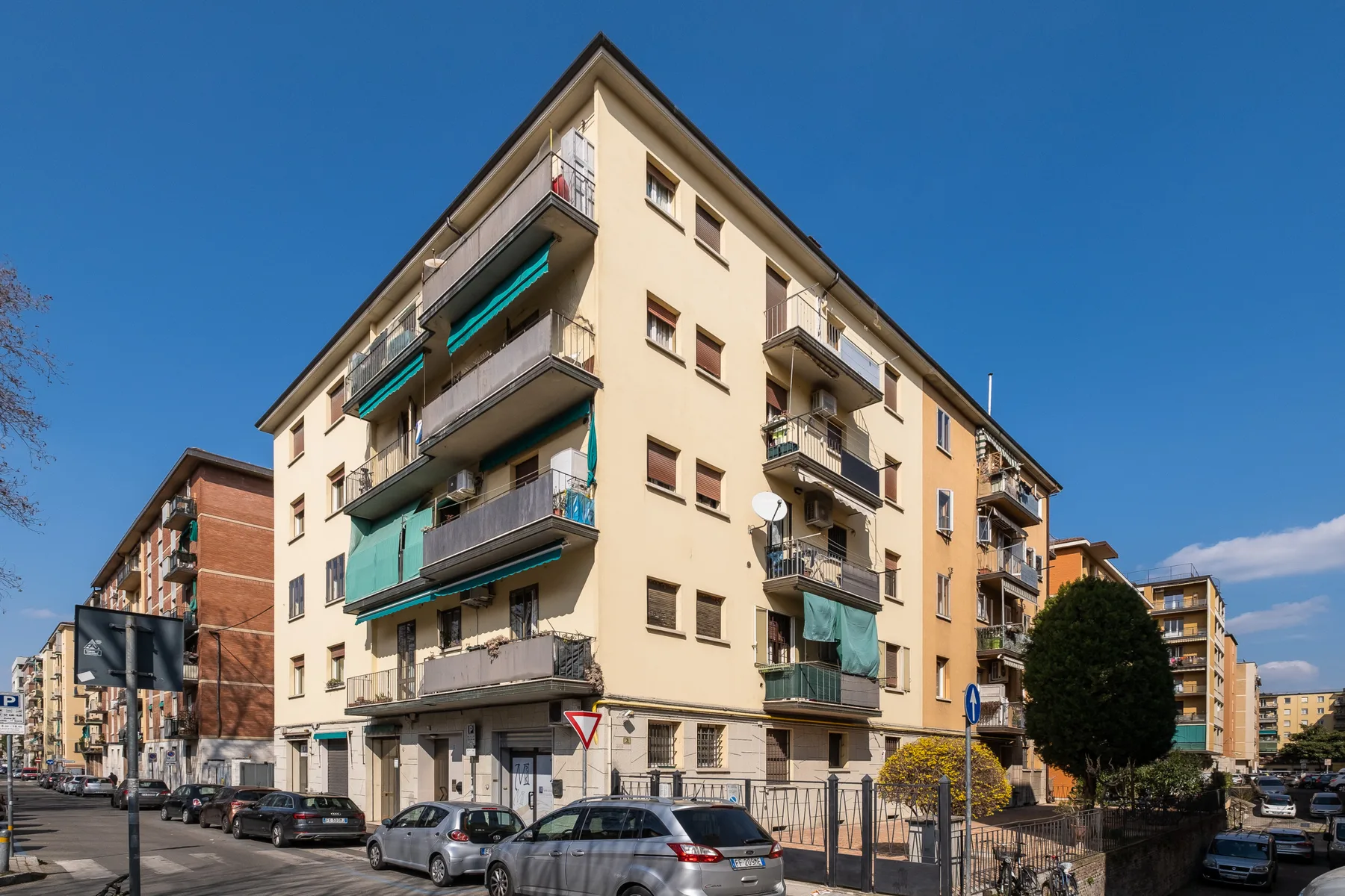 Un edificio de apartamentos de varias plantas se alza junto a una calle con coches aparcados.