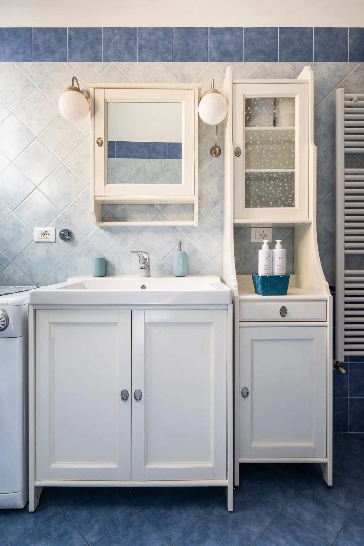 Un mueble de baño con lavabo y armarios con espejo frente a paredes revestidas de azulejos.