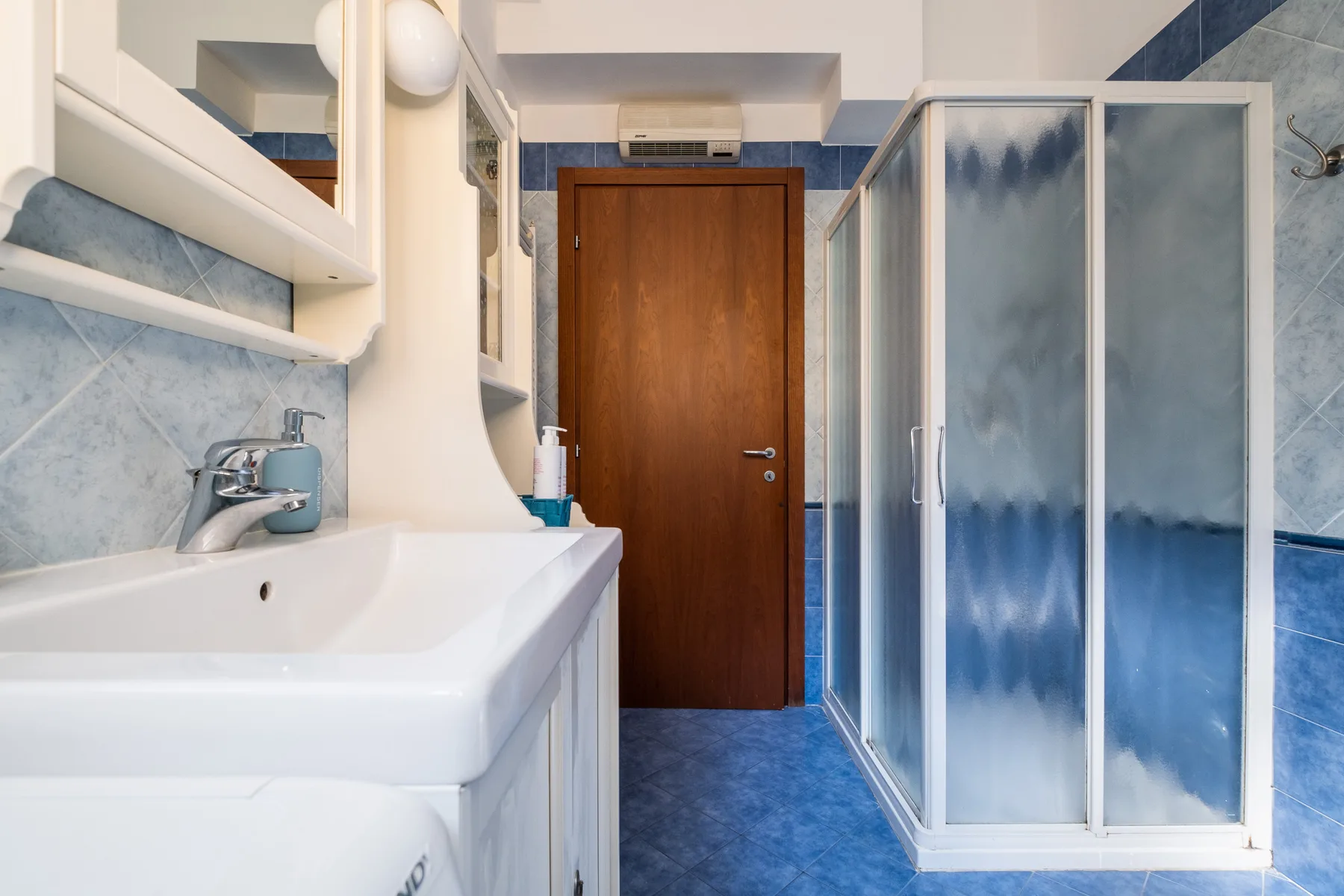 Un baño con lavabo, ducha y una puerta de madera.