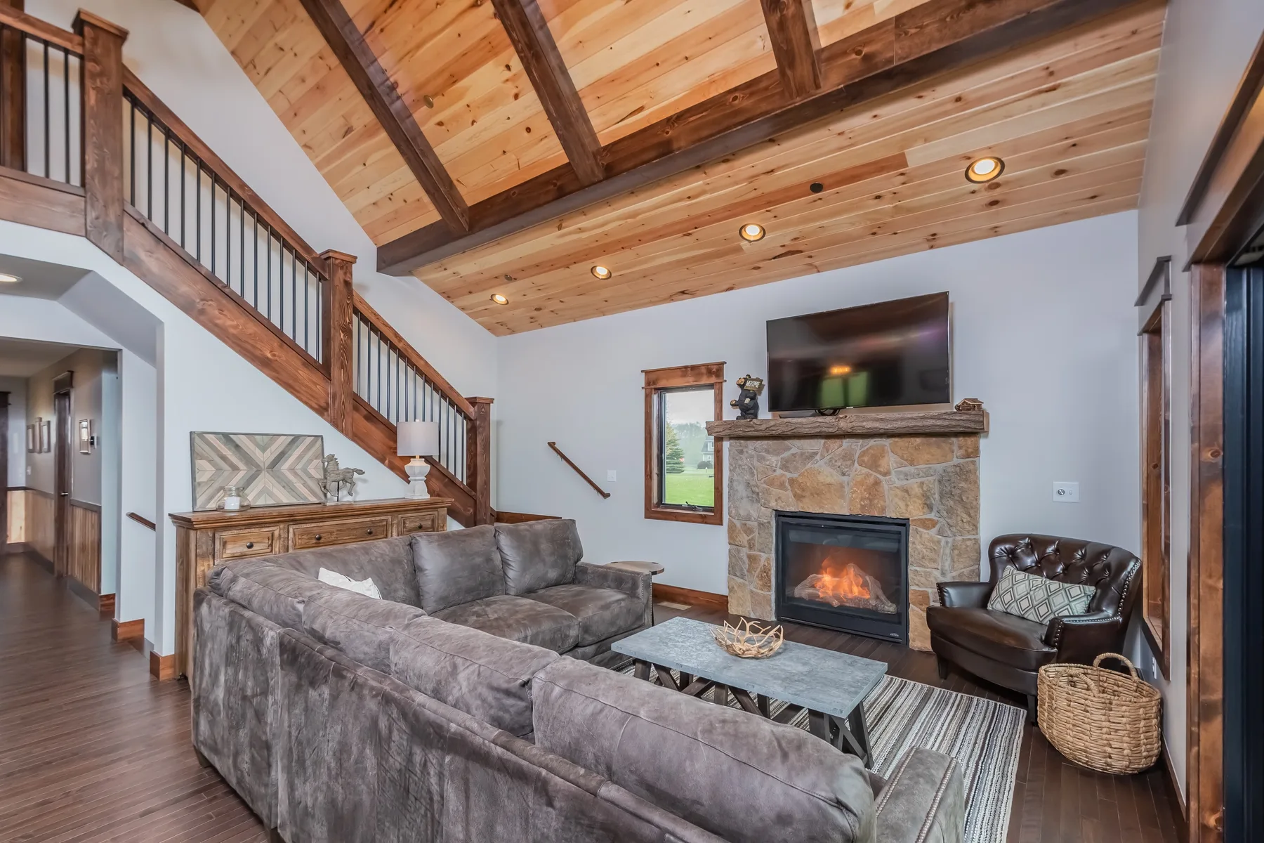 Sala de estar con asientos seccionales, chimenea de piedra y techo con vigas de madera.