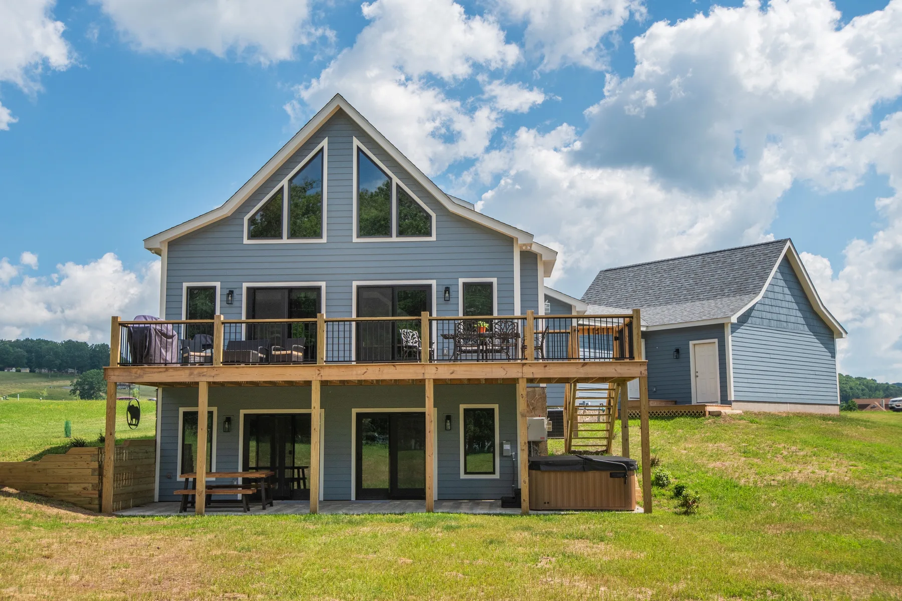 A large gray house with a wooden deck stands in an open grassy landscape.