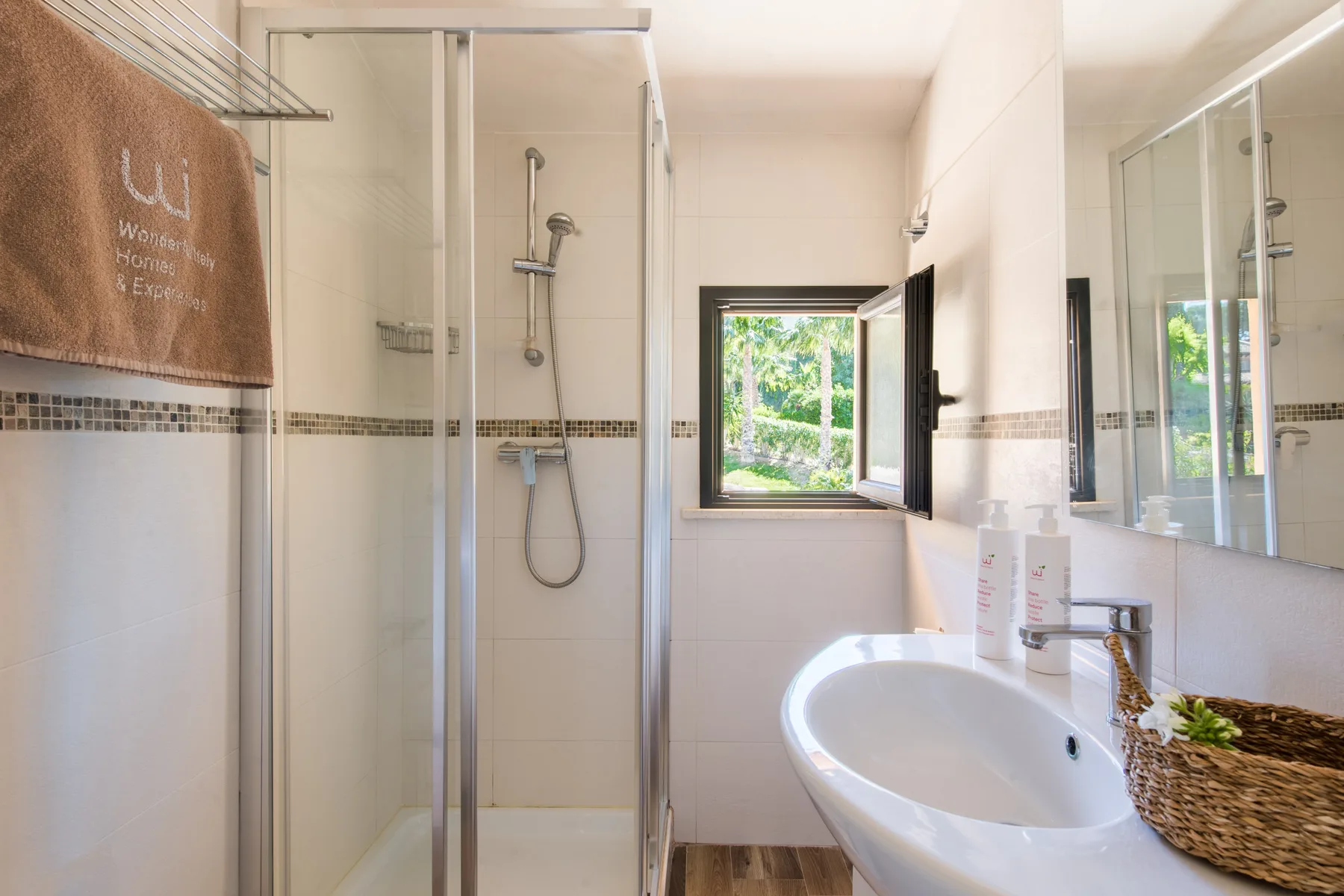 A bright bathroom with a glass shower, sink, and open window.