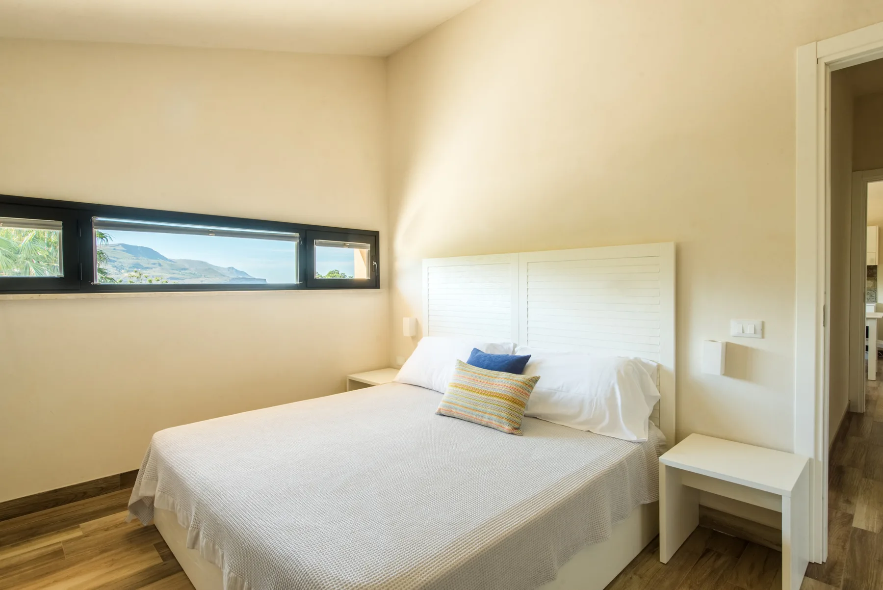 A bedroom with a bed beneath a long horizontal window.