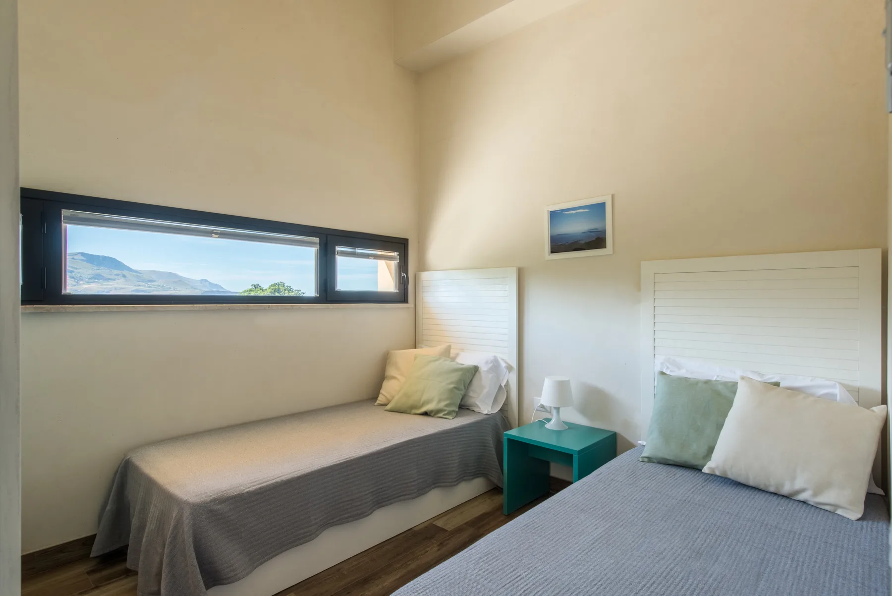 A bright bedroom with two beds and a long horizontal window.