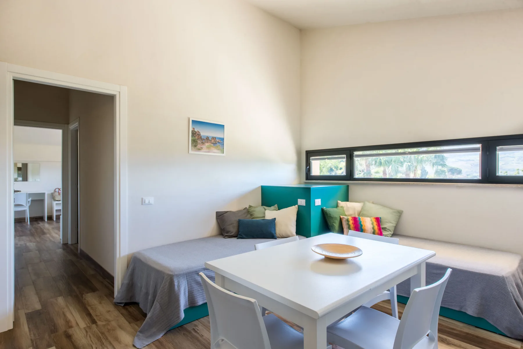 A bedroom with beds arranged along the wall beneath a long horizontal window.