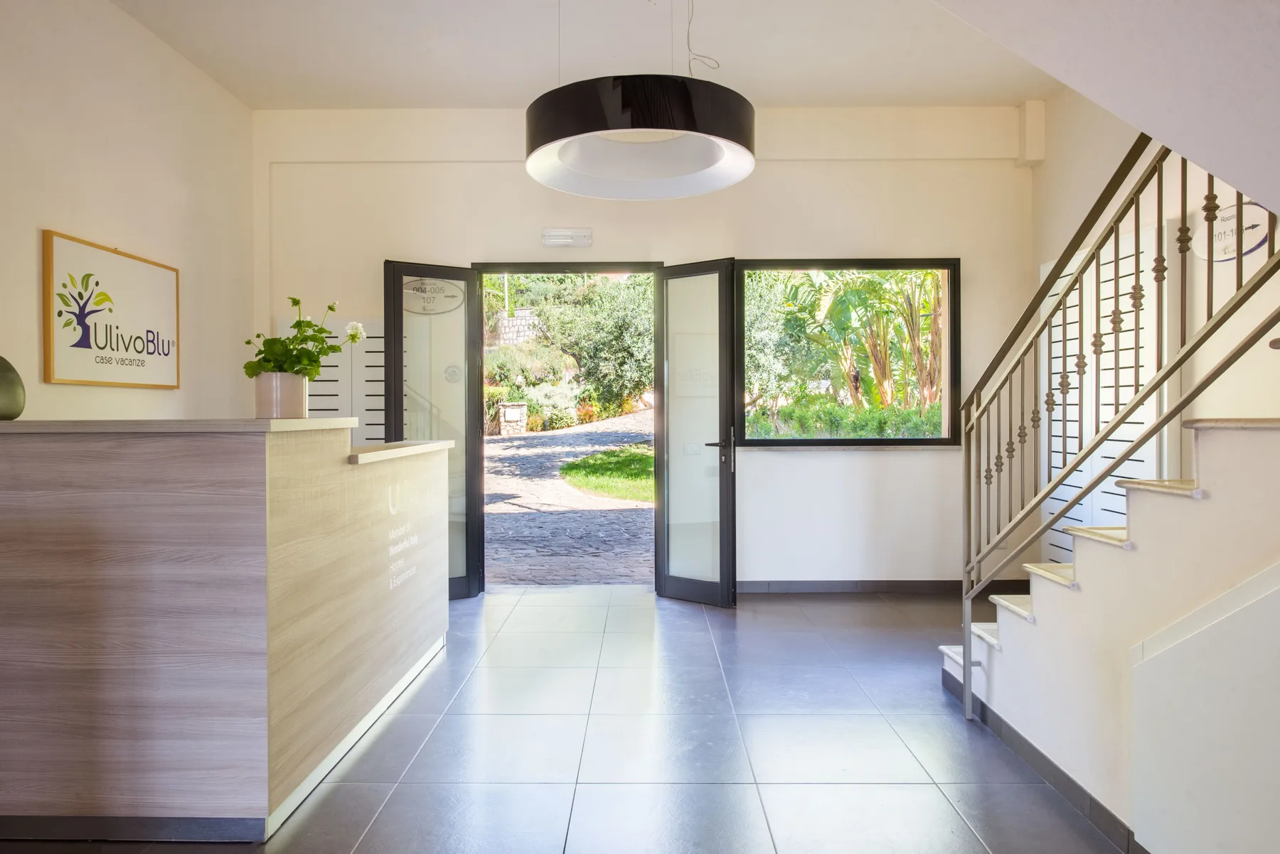 A bright reception area with a front desk, open entrance, and staircase.