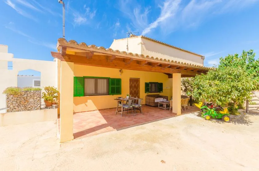 A covered patio with outdoor seating and green shutters beside a sunny courtyard.