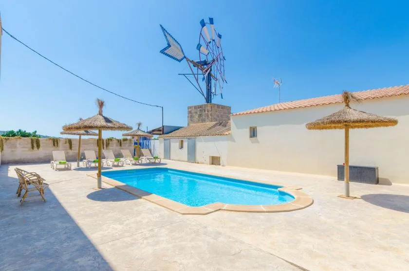 An outdoor swimming pool sits beside white walls and thatched parasols.