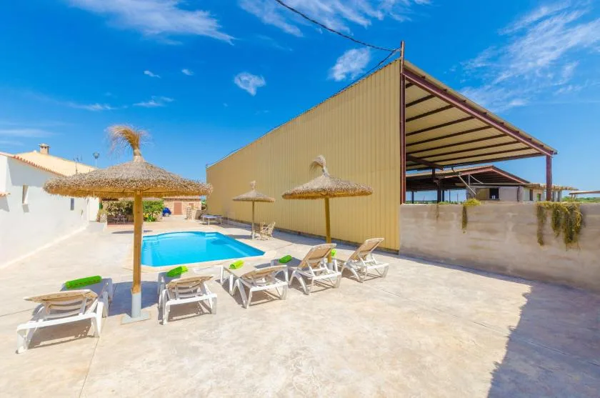 An outdoor swimming pool is surrounded by lounge seating and thatched parasols.
