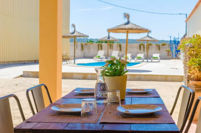 A shaded outdoor dining table overlooks a swimming pool and sun loungers.