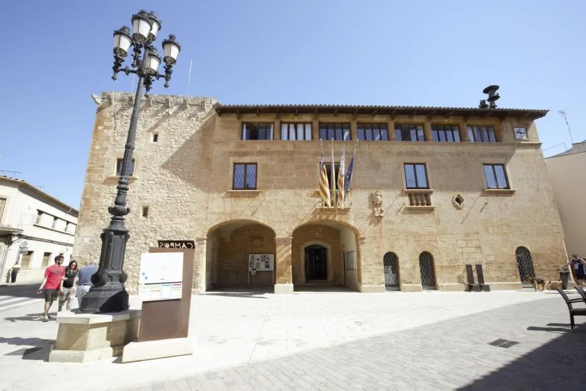 A stone civic building faces a paved plaza beneath a clear sky.