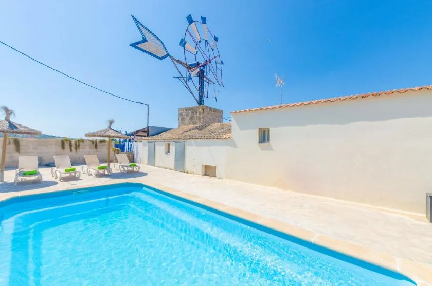 A swimming pool sits beside a white building, with lounge seating along the far side.