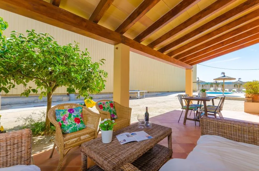 A covered patio with wicker seating and a dining table overlooks an open outdoor area.